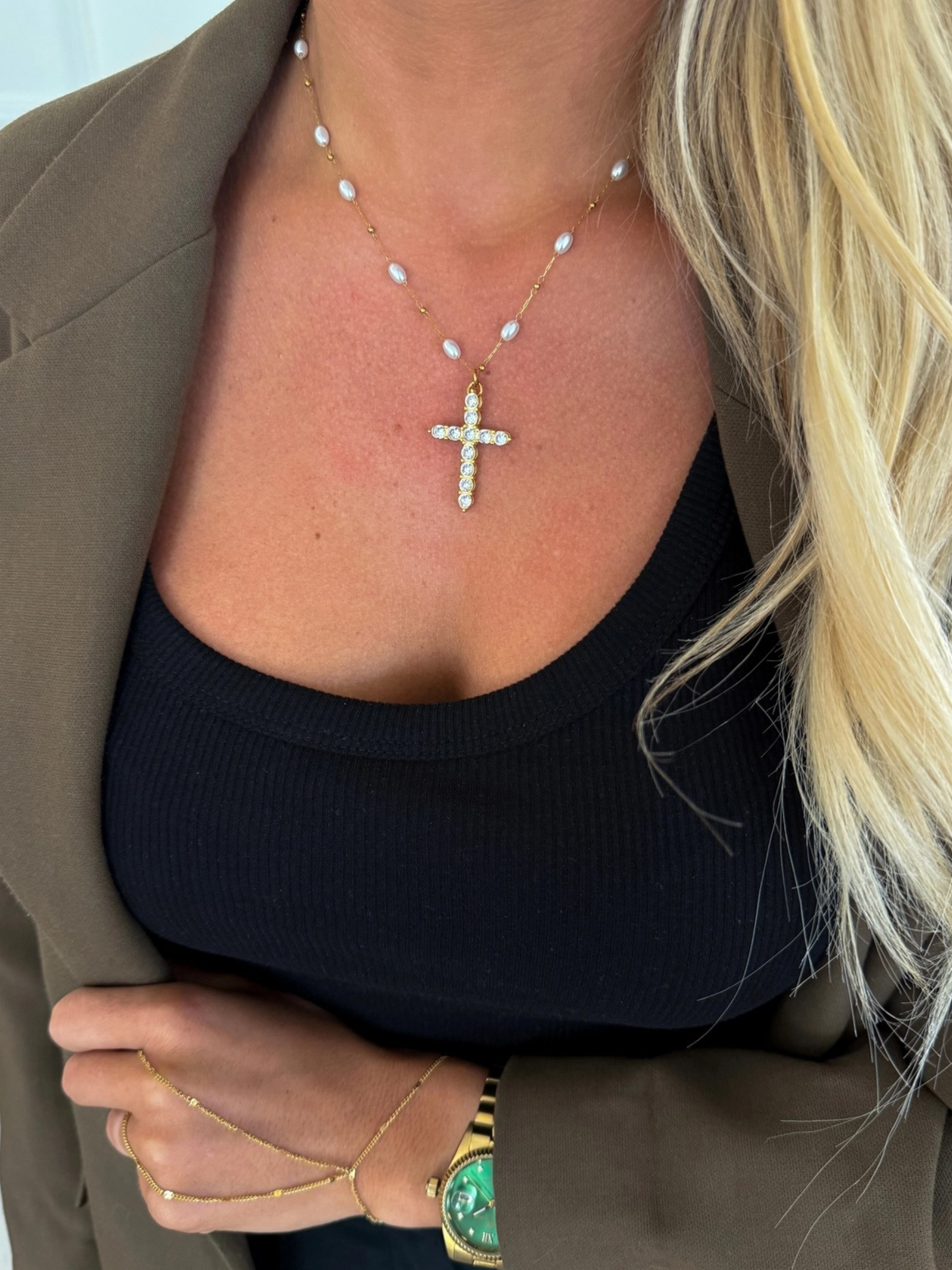 Person wearing a necklace with a cross pendant, gold bracelet, and green gemstone ring.